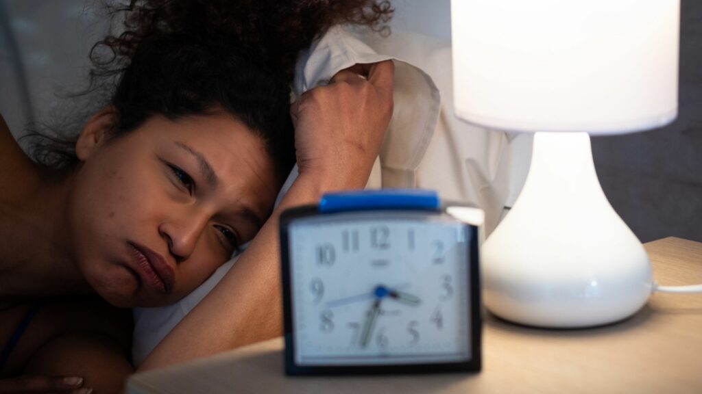 Middle aged woman can't sleep, she lies in bed staring at a clock that reads 3:30 am
